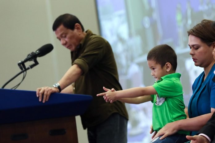 POSE LIKE A PRO: Stingray, the grandson of President Rodrigo Duterte (in green polo) pose like enjoying his fingers holding a gun while his grandfather talks about imposing stiffer government regulations to gun buyers.-PHOTO: PPD POSING LIKE A PRO: Stingray, the grandson of President Rodrigo Duterte (in green polo) pose like enjoying his fingers holding a gun while his grandfather talks about imposing stiffer government regulations to gun buyers.-PHOTO: PPD